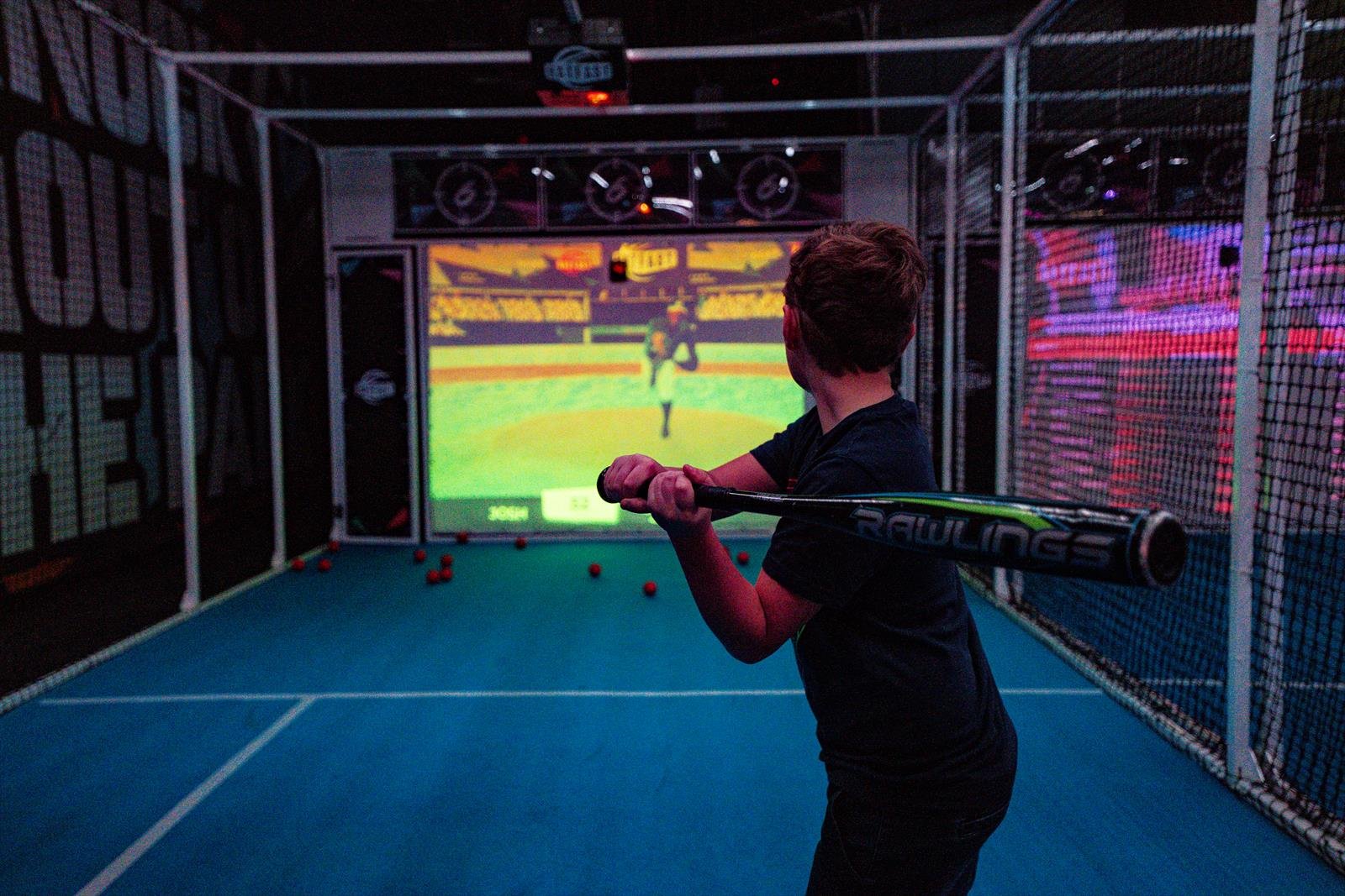 A batter squares up to a pitch on the big screen in a baseball batting cage