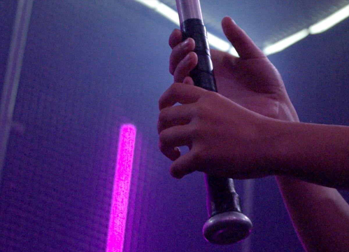 Close-up of hands gripping a baseball bat with neon light behind