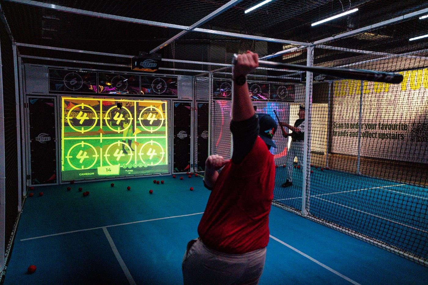 A batter swings at a pitch on the big screen in a batting cage