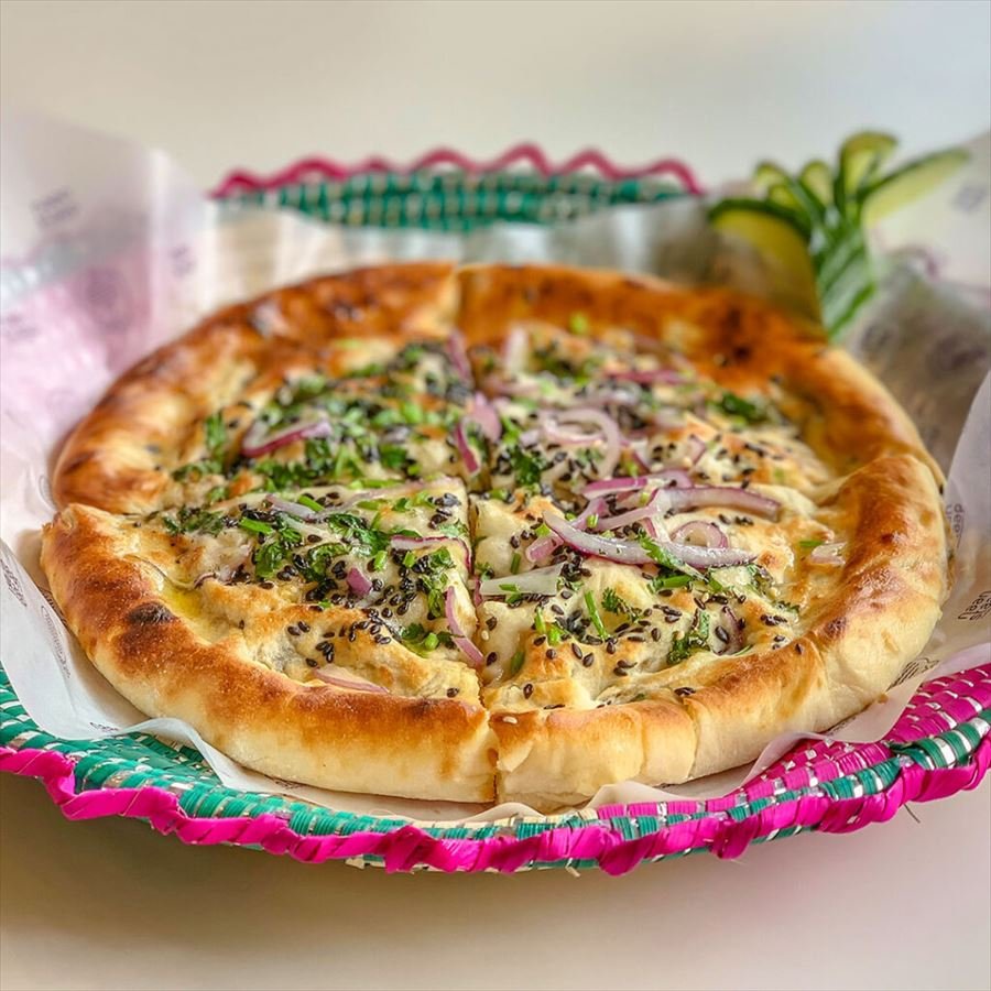 A freshly baked stuffed naan topped with red onion and herbs