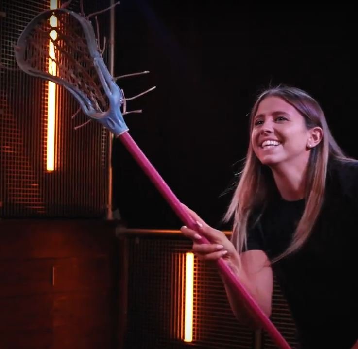 A smiling player cradles a lacrosse stick under orange lights
