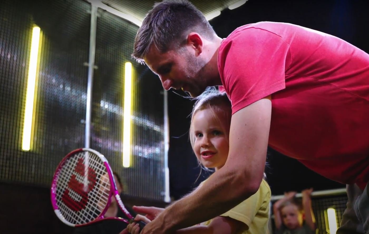 A father helps his young daughter line up a tennis shot